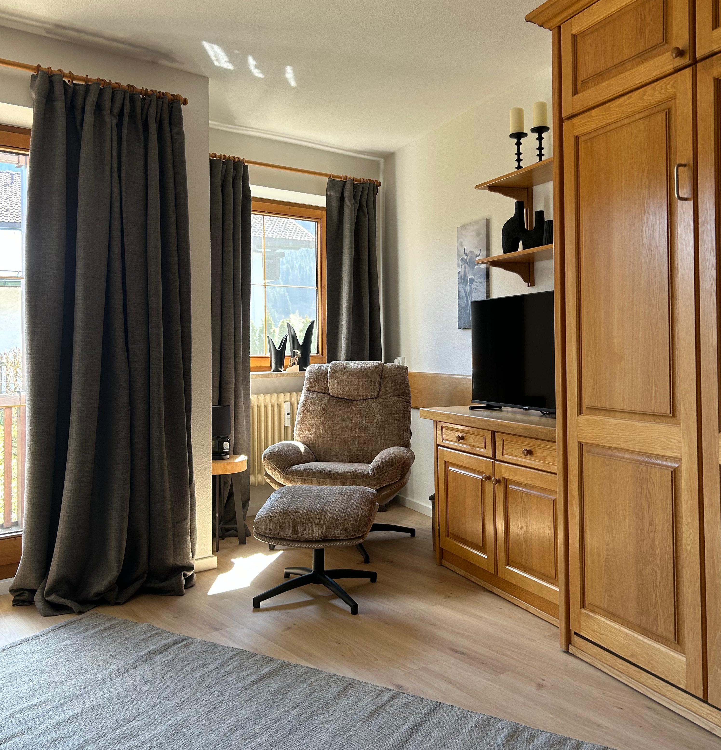 Heller Wohnbereich mit gemütlichem Lesesessel, Schrank und Blick zum Balkon