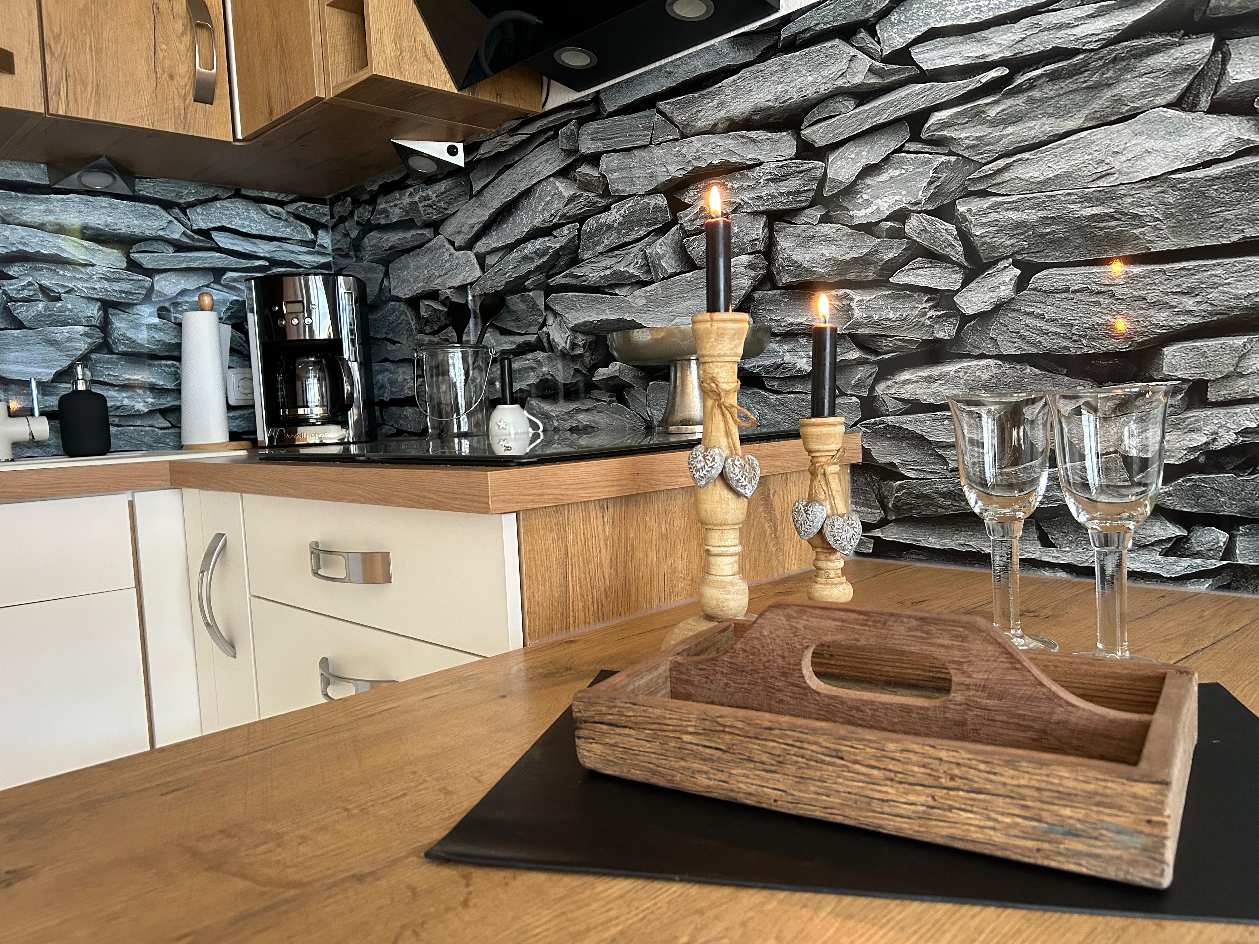 Moderne Holzküche mit Natursteinwand-Optik, Kaffeemaschine und liebevoller Tischdekoration aus Holzkerzenständern und Weingläsern
